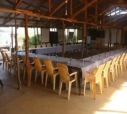 A large open hall with long tables laid in a U shape under a timber roof, with plastic chairs around the tables.