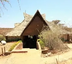 A thatched building with a steep A-frame entrance, low stone walls and a sandy path, under a blue sky.