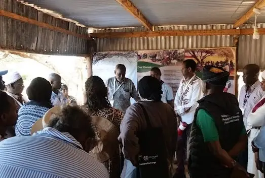 A group of visitors stands inside the open museum shed while a guide speaks, with display boards behind them.